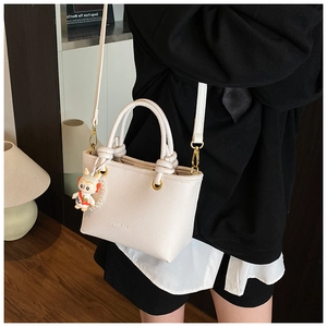 Close-up of beige lychee leather handbag with knot handles and cute rabbit charm