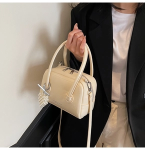 Detail of a beige pillow bag with pearl charm and Fashion & Bags text on textured leather