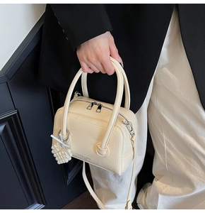 Detailed shot of beige Boston bag with pearl heart charm and elegant bow decoration
