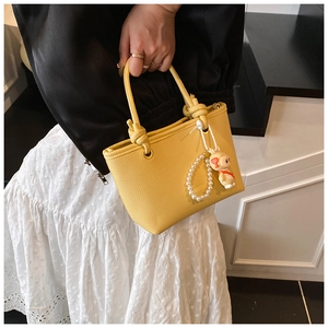 Close-up of bright yellow leather tote bag with pearl chain and cute rabbit charm