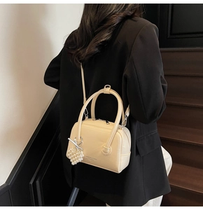 Model wearing a cream Boston shoulder bag with pearl pendant over a black blazer