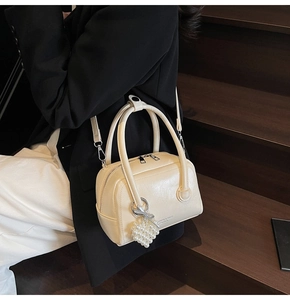 Detail of cream glossy handbag with pearl heart charm and adjustable shoulder strap