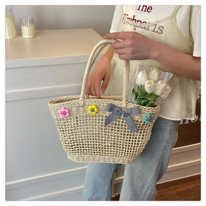 Detail shot of woven straw handbag featuring colorful floral accents and checkered bow