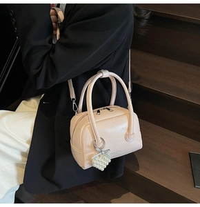 Detail of a beige leather boston bag with pearl grape charm and adjustable shoulder strap
