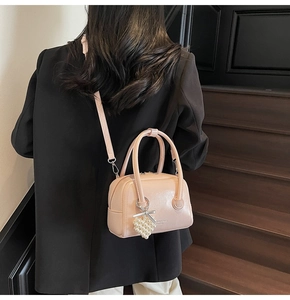Detail of light pink mini Boston bag with glossy finish and pearl heart charm on a black blazer