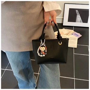 Close-up of black lychee texture bucket bag with astronaut charm and pearl chain