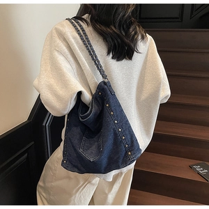 Detailed view of the woven denim chain strap and metal rivet studs on the tote bag