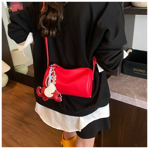 Detail of red cylinder bag in litchi leather with a cute elephant pendant on a model