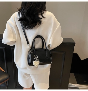Close-up of black matte leather Boston bag with white text and pearl heart charm detail