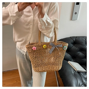 Detail of hand-woven straw tote bag with floral accents and a gingham bow on a model