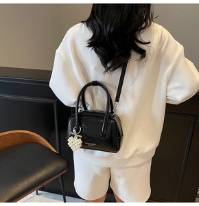 Detail of black patent leather crossbody bag with white pearl heart pendant on model