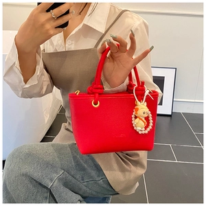 Close-up of red lychee textured leather bucket bag with braided rope handle and charm