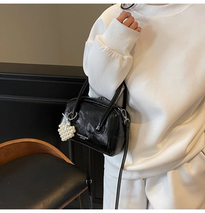 Detail of black textured leather boston bag with pearl heart charm and shoulder strap