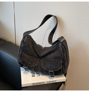 Close-up of black washed denim underarm bag featuring dual utility pockets with buckles