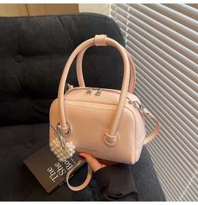 Pink lychee grain leather mini handbag with pearl heart charm on a black sofa