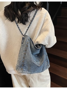 Blue denim tote bag with gold rivets and chain strap worn by a model on stairs