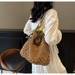 Detail of straw woven hobo bag with hollow pattern and colorful ethnic strap on white dress