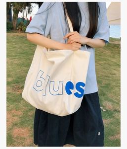 Grand sac cabas en toile beige avec lettrage bleu présenté en extérieur décontracté