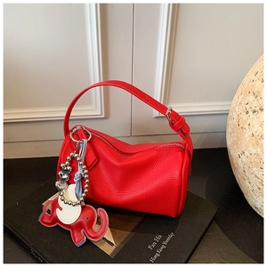 Detail of red lychee grain leather cylinder bag with elephant charm on black books