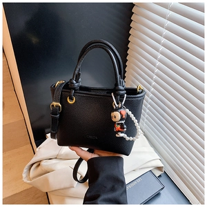 Detail of black litchi grain bucket bag with pearl charm and adjustable shoulder strap
