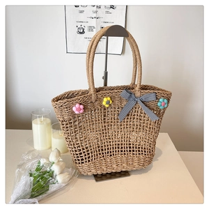 Detail of straw woven tote bag featuring colorful floral appliques and a checkered bow tie