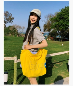 Photo lifestyle d'un grand sac fourre-tout en toile jaune avec lettrage bleu sur une pelouse verte