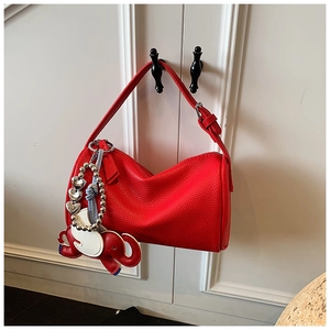 Detail view of red pebble leather boston bag featuring a designer elephant pendant accessory