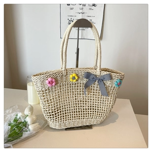Detail of straw woven tote bag featuring colorful plush flowers and a checkered bow