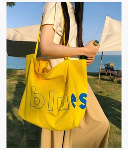 Détail d'un sac cabas en toile jaune avec lettrage bleu sur un fond extérieur pittoresque
