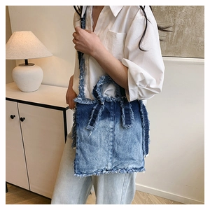 Détail d'un sac cabas en jean dégradé avec bords effilochés porté par un mannequin chic