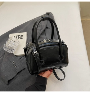 Detail of black glossy leather pillow bag placed on a grey suit with fashion accessories