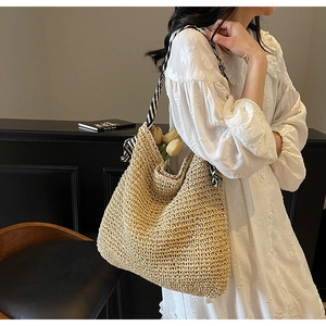 Detail view of woven straw tote bag featuring black and white striped fabric handles