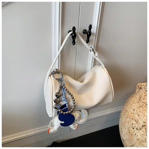 Detail of white lychee leather boston bag with a colorful elephant charm on a cabinet
