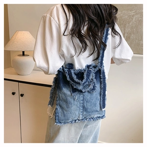 Détail des bords effilochés et des franges sur ce sac à bandoulière en denim délavé