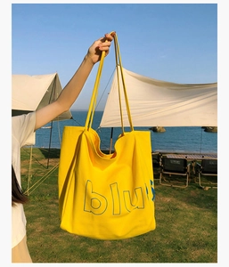 Détail d'un sac cabas en toile jaune avec lettrage bleu dans un décor de camping côtier