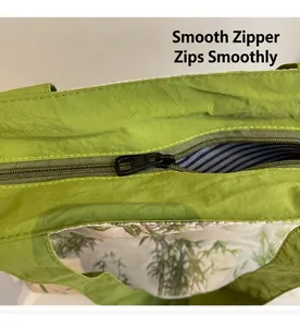 Close-up of a green canvas tote bag showing smooth zipper closure and printed lining