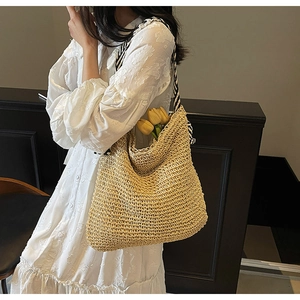 Close-up of a woven straw tote bag with black and white striped ribbon shoulder straps
