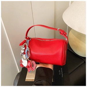 Detail of red cylinder bag in litchi grain leather with cute elephant charm and silver chain