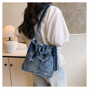 Détail du sac à épaule en jean bleu clair avec bords effilochés et un grand nœud décoratif