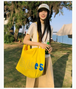 Détail du sac cabas en toile jaune avec lettrage bleu dans un cadre de vie en plein air