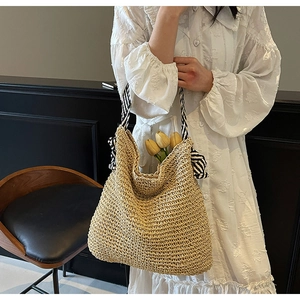 Detail of straw woven tote bag with black and white striped handles and ribbon accents