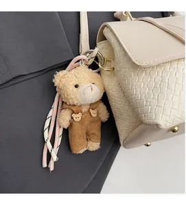 Nahaufnahme eines Plüschbären-Anhängers mit Latzhose an einer strukturierten Handtasche