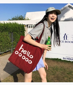 Donkerrode canvas shopper met witte hello-letters gedragen door een model in de buitenlucht