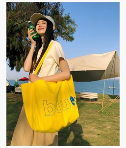 Gros plan du sac cabas en toile jaune vif avec lettrage bleu sur une plage ensoleillée
