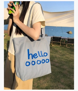 Lifestyle buitenopname van een lichtblauwe canvas draagtas met hello ooooo belettering