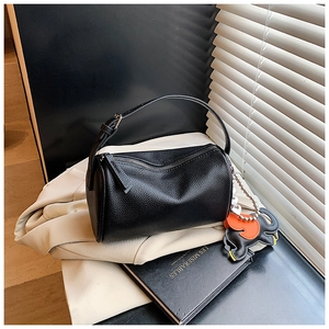 Detail of black cylindrical handbag in lychee leather texture with elephant charm accessory