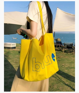 Détail du sac cabas en toile jaune avec lettrage blue bleu sur une pelouse ensoleillée