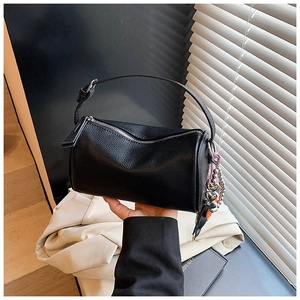 Detail of black cylinder bag in lychee leather featuring a heart charm and top handle