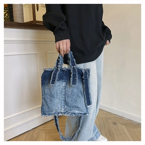 Détail du sac cabas en jean dégradé bleu avec bords effilochés et texture délavée rustique