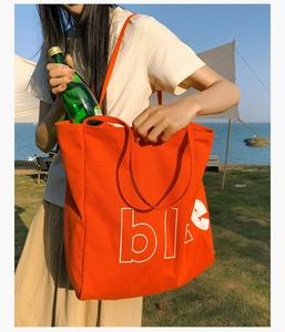Détail d'un grand sac cabas en toile orange avec lettrage blanc sur de l'herbe